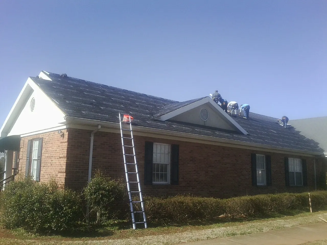 Crew tearing shingles off a brick ranch roof with a ladder set — Metal Roof Repair work by our crew in Woburn