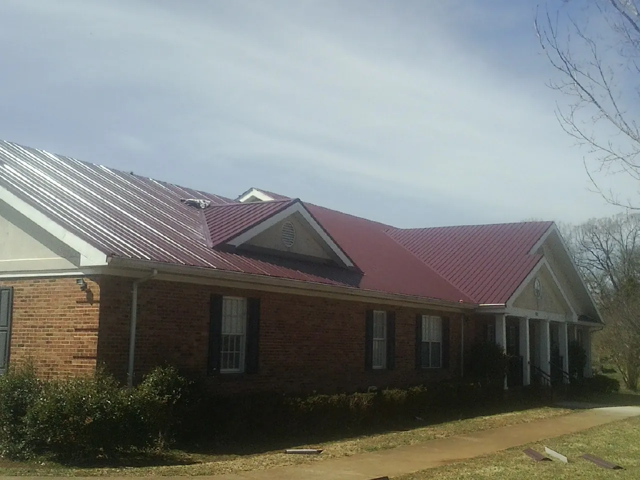 Red metal roof with gabled entries on a long brick building, from a Hail Damage Roof Repair job in Woburn