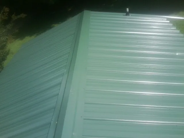 New green metal panels meeting at the ridge of a roof — Flat Roof Repair work by our crew in Woburn