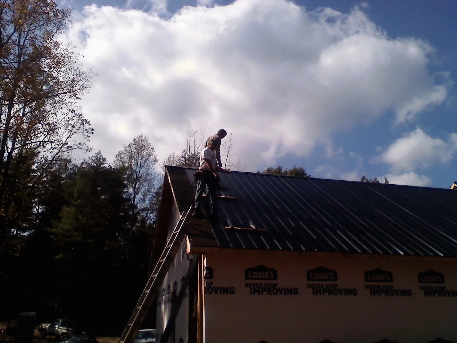 Roofer fastening dark metal panels high against a cloudy sky, from a Roof Inspection job in Woburn