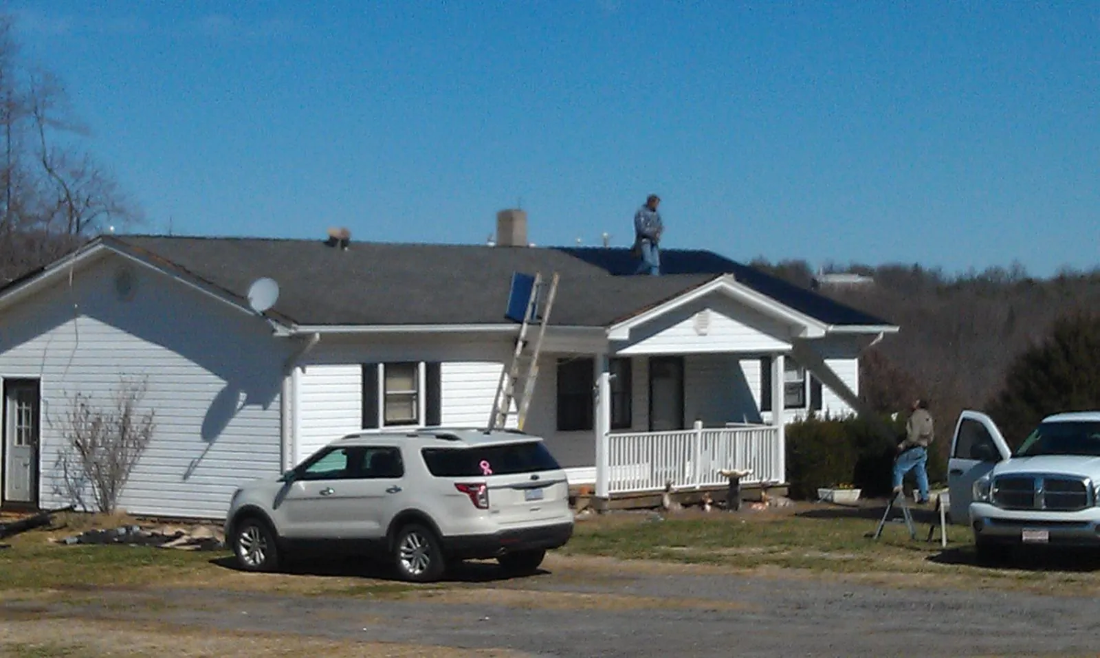 Roofers stripping shingles from a white ranch house roof in Woburn