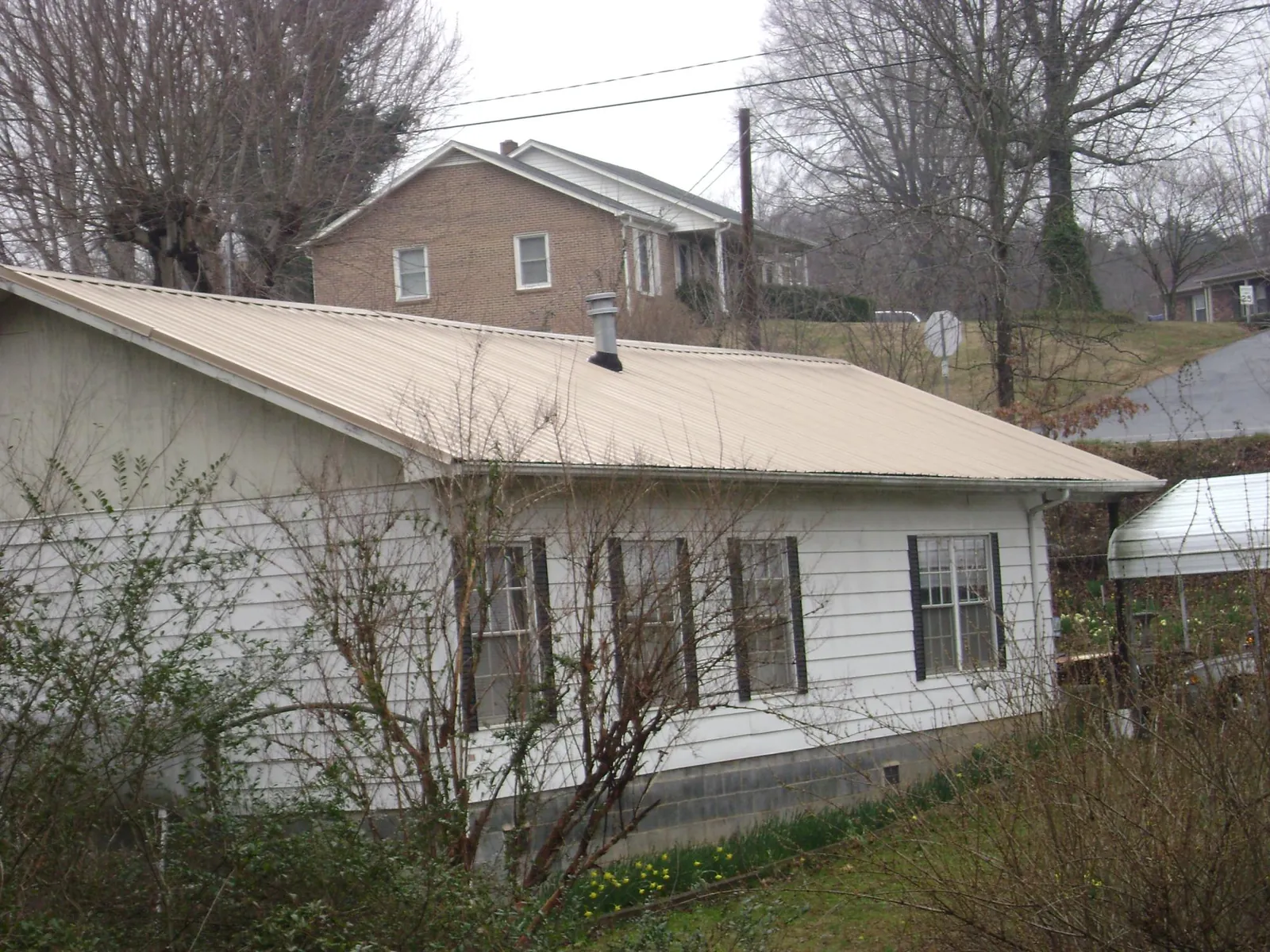 Tan metal roof on a white sided house set into a hillside — Commercial Roofing by Roofing Brothers in Woburn